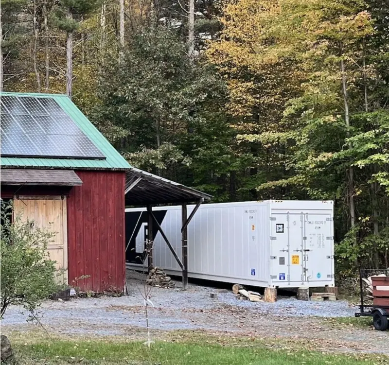 White Freight Farms shipping container farm installed beside a solar-roofed barn