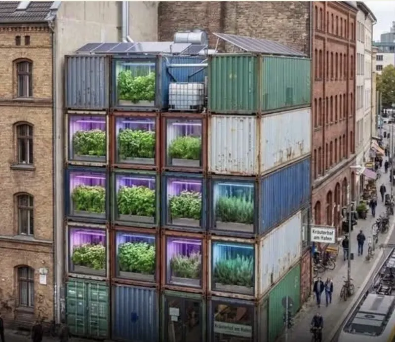 Stacked shipping container vertical farm growing herbs in a dense city neighborhood